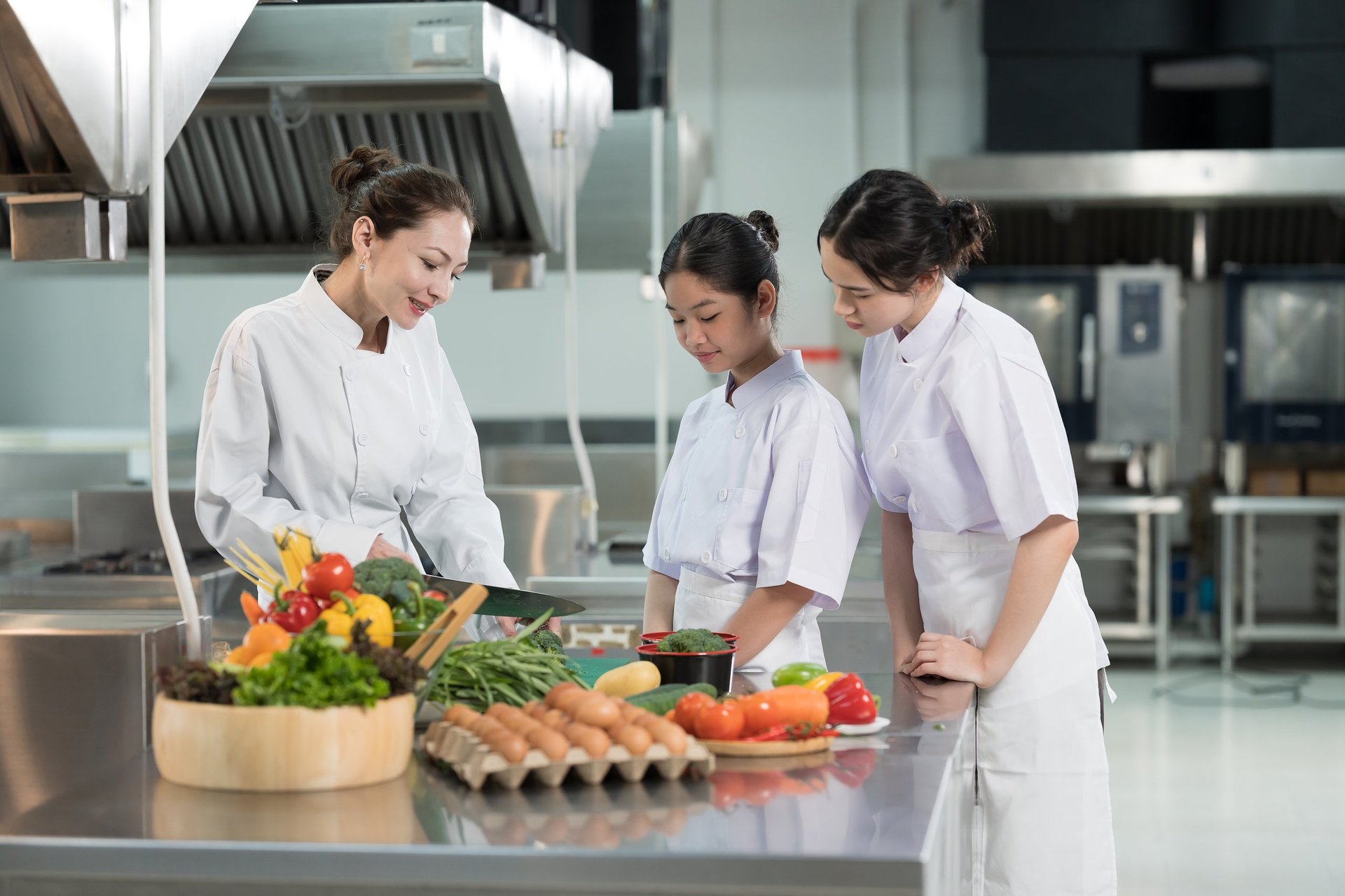 Group of young chefs wearing white aprons during food preparation and learning cooking in kitchen