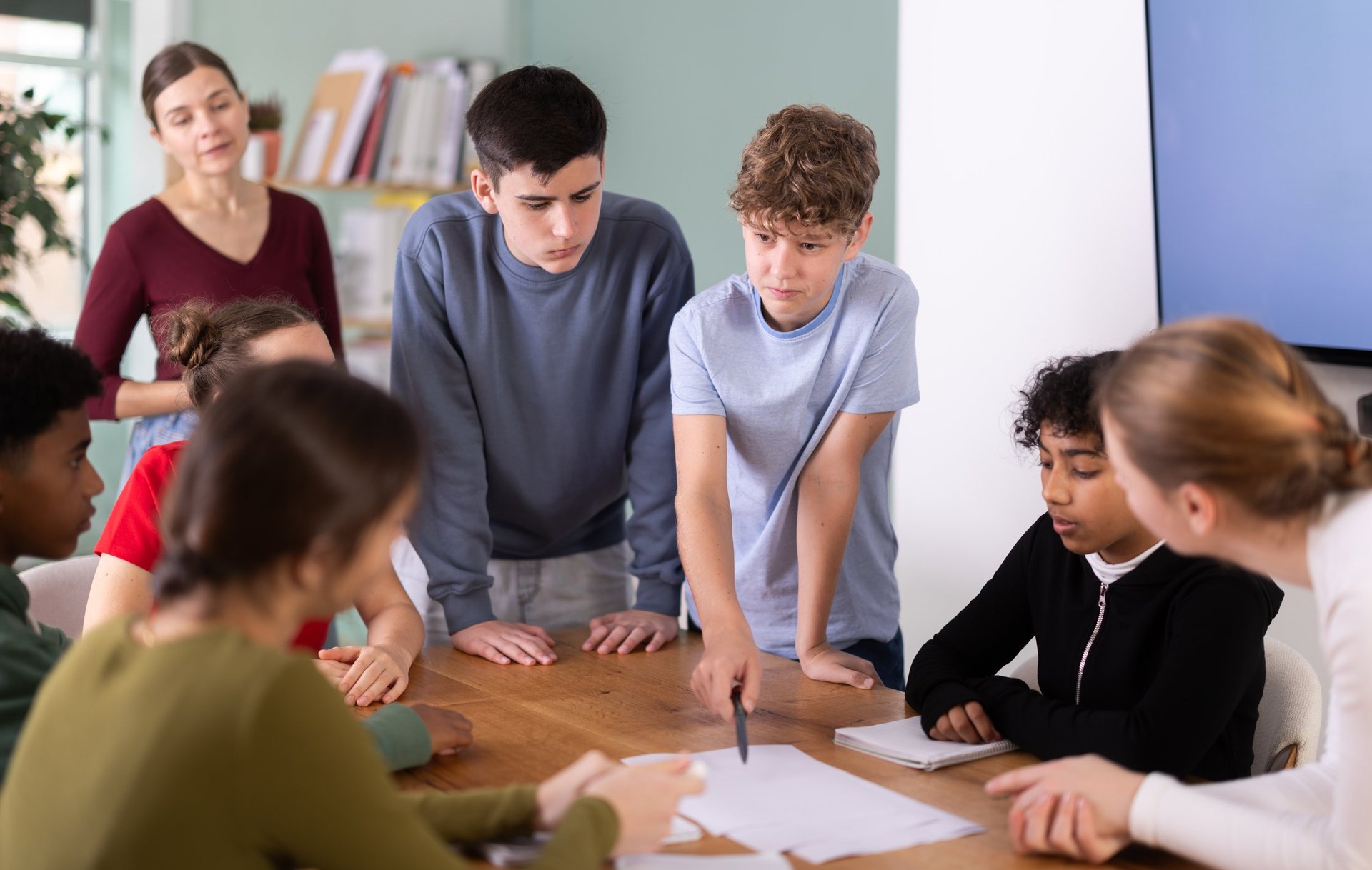 Group of teenagers and students discussing tasks at a table, exchanging opinions in a classroom setting
